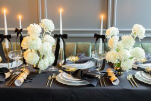 Elegante Tischdeko für Silvester in Schwarz und Gold mit floralen Akzenten und edlem Geschirr für eine festliche Atmosphäre.