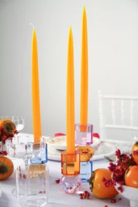 Stick candles in crystal candle holders from EJA, embedded in a table decoration with fruit.
