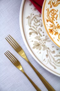 Gold-coloured cutlery and hand-painted plates from the Adelasia collection on white linen table linen.