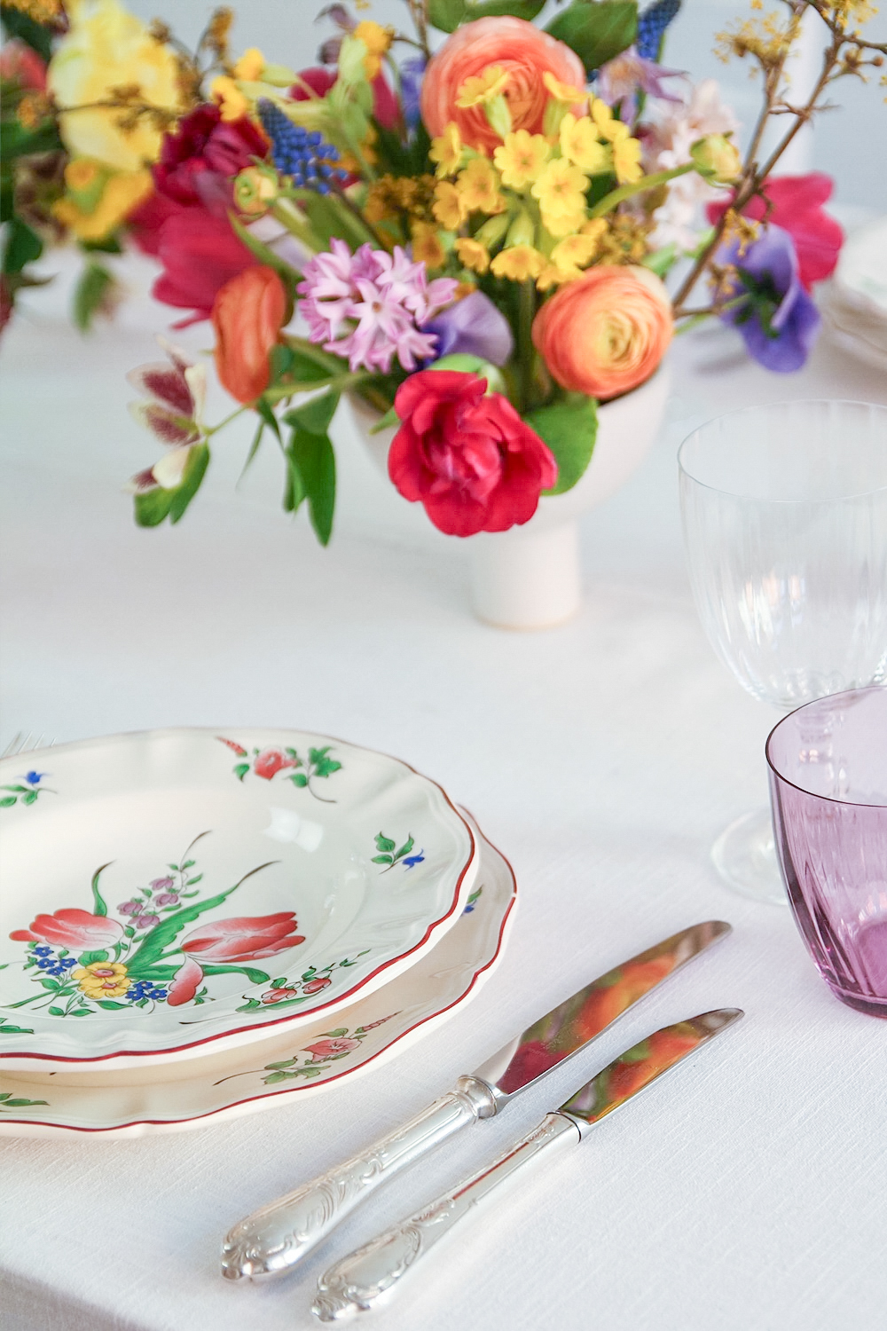 Vintage-Besteck mit floralen Griffen neben einem Teller mit Blumenmuster und lila Glas