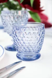 Close-up of the Villeroy & Boch Boston blue water glass on a white table with red peonies in the background.