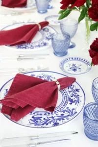 Place setting with Adelasia Blu plate, red linen napkin and Doric Clear cutlery on a white tablecloth.