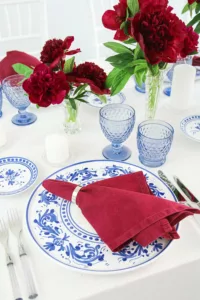 Covered plate with blue and white decoration, wine-red napkin and blue glasses in elegant summer decoration.