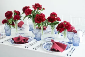 Table decoration with red peonies, blue glasses and hand-painted crockery in blue and white.
