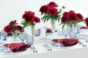 Summery table with peonies, blue glasses and hand-painted crockery in red and blue.