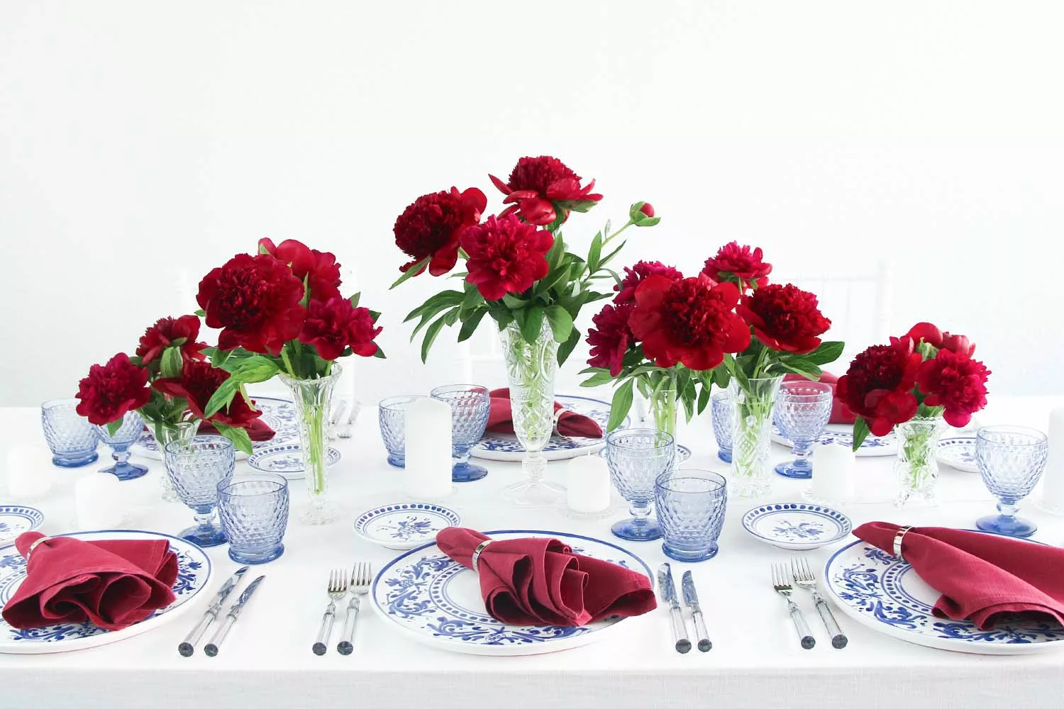 magnolias-on-silk-table-of-the-month-mai-peony-red-blue-table-inspiration-9 Generously laid table with red peonies, blue glasses and blue and white crockery on a white tablecloth.