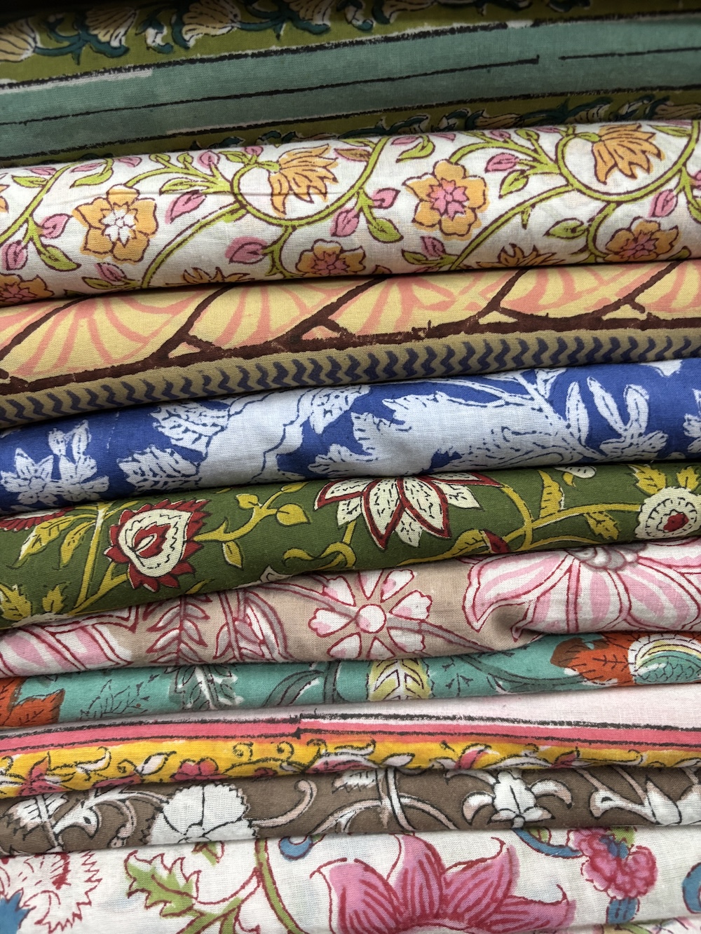 Stacked hand-printed block print fabrics from Jaipur in floral patterns and bold colours, showcasing tactile textures and artisanal techniques.