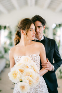 Bridal couple with a cream-coloured bouquet of roses against a floral background at the Reference Masterclass