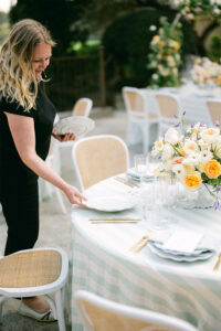 Irka arranges plates and crockery at a round table with a striped tablecloth